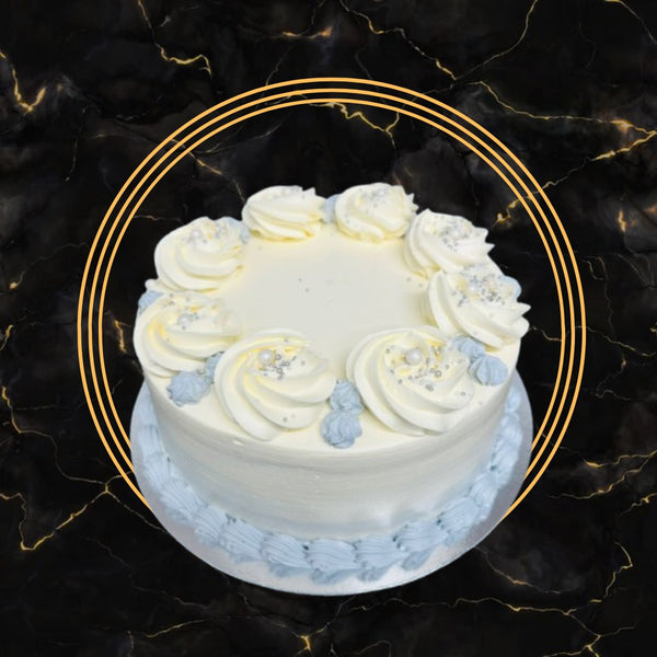White buttercream cake with blue frosting accents and silver pearls made by The Bakers Shop Birmingham.